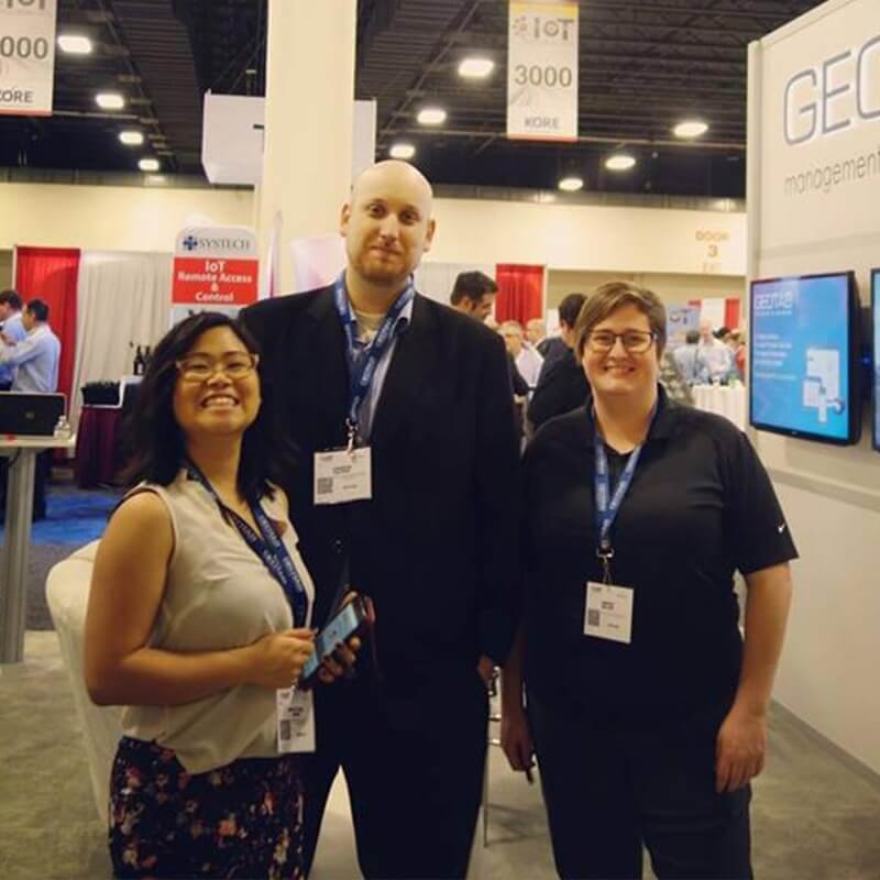 Three people standing in front of a Geotab booth at a convention