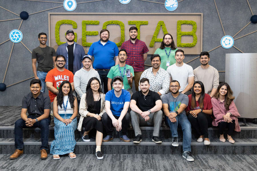 Smiling geotabbers stand in three rows on a gray background with the big geotab logo.