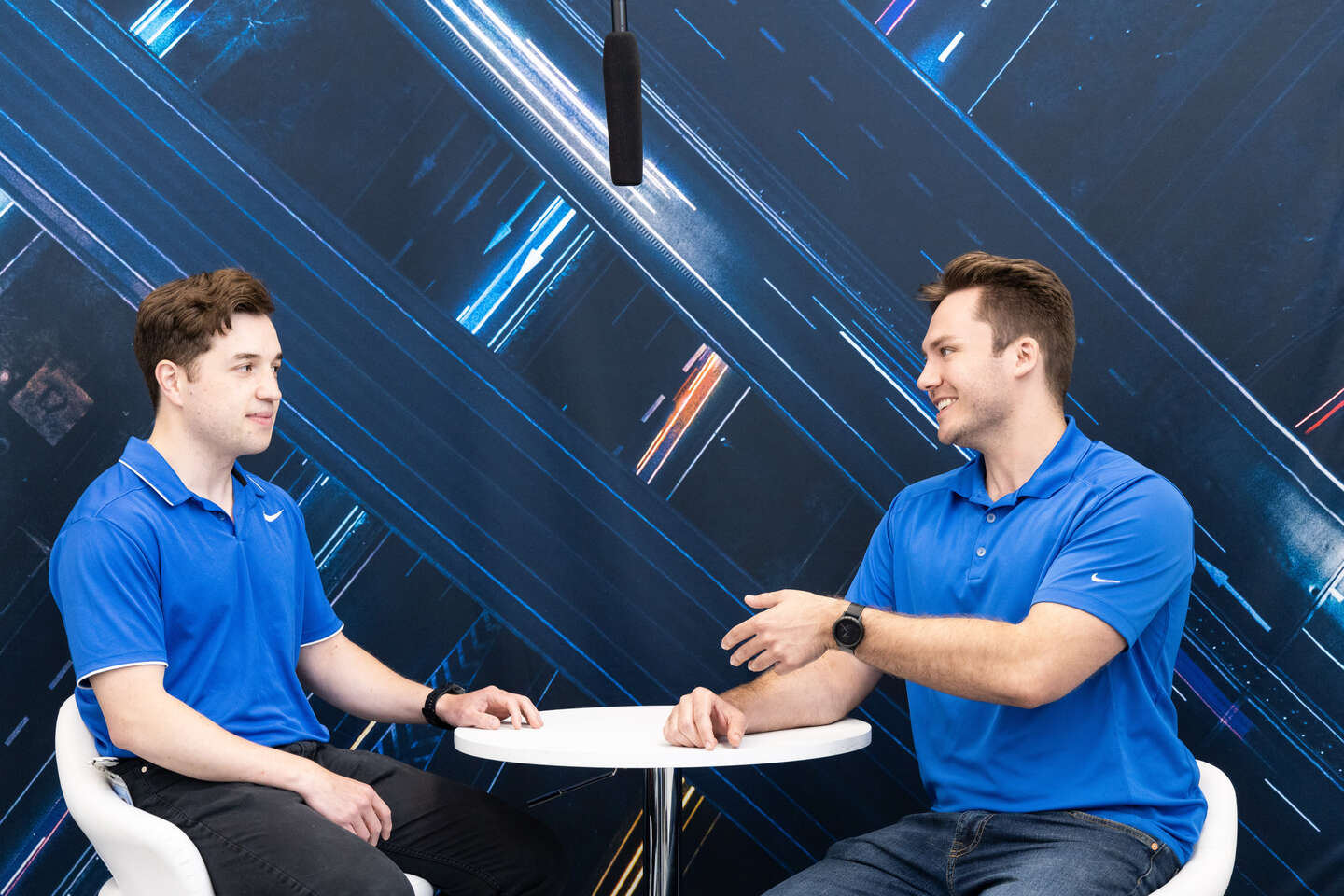 Two geotabbers in blue t-shirts sit opposite each other and one extends his hand for a handshake